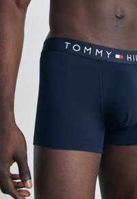 Sötétkék boxer alsó, puha anyagból készült, széles gumis derékrészével, amelyen fehér és piros színű "TOMMY HILFIGER" logó található.