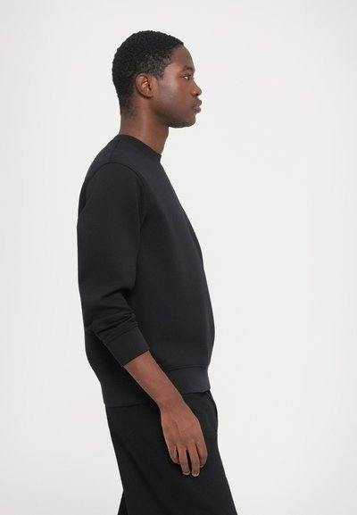 Svart sweatshirt med rund halsringning, långa ärmar och ribbstickade mudd. Slät textur, figurnära passform, kombinerad med matchande svarta byxor.