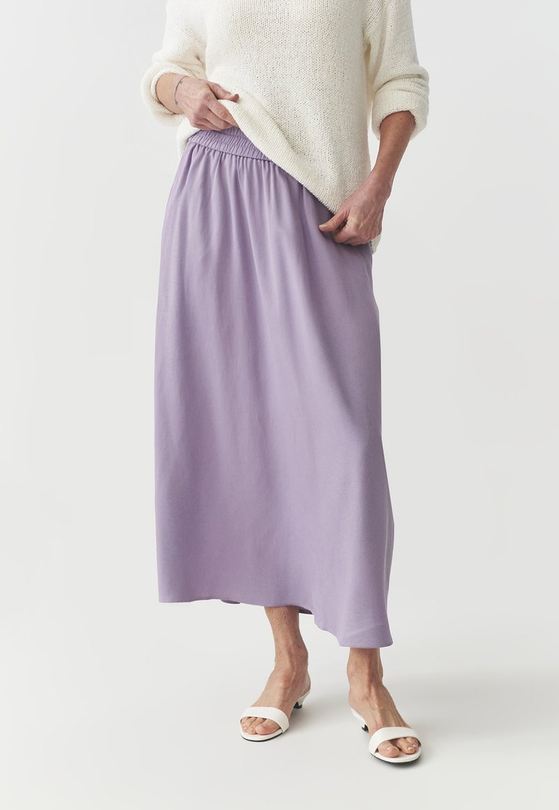 Gonna maxi in lavanda con vita arricciata, abbinata a sandali bianchi con punta aperta. Tessuto morbido con texture liscia, design fluido.