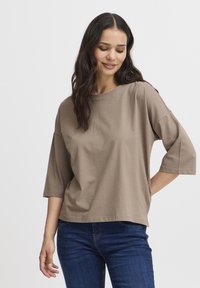Brun, kortærmet t-shirt lavet af bomuld med en afslappet pasform og rund halsudskæring, parret med mørk denimjeans.