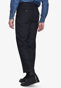 Sorte bukser lavet af glat stof, med lige ben, manchetkant og to baglommer. Sættes sammen med sorte loafers.