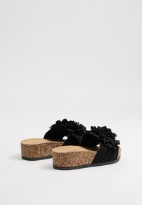 Chanclas negras con suela de plataforma de corcho. Cuentan con una parte superior de ante y detalles florales texturizados en la correa.
