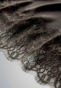 Černá krajka s květinovými a geometrickými vzory přes hladkou tmavou tkaninu, ukazující jemnou síťovinu a delikátní texturu.