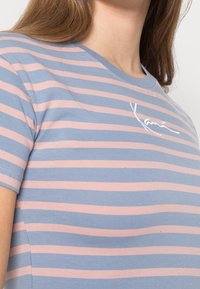 Camiseta de rayas en algodón azul y rosa, con cuello redondo y nombre de la marca bordado en blanco en el lado izquierdo.