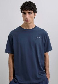 Camiseta de algodón azul marino con mangas cortas, escote redondo y un pequeño logotipo bordado en blanco en el pecho. Textura suave.