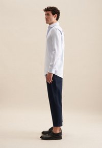 Camicetta azzurra chiara con maniche lunghe, abbinata a pantaloni blu scuro e scarpe nere. La camicia presenta un colletto strutturato e fessure laterali.