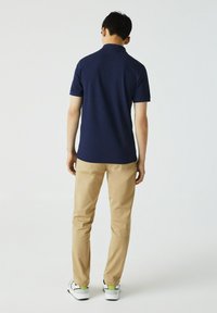 Polo à manches courtes marine, coupe décontractée, associé à un pantalon beige. Chaussures blanches avec des accents verts. Design simple, texture lisse.