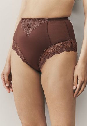 Kõrge vöökohaga pruunid püksikud lillelise pitsist detailiga vöökohal ja sääreavades, mida kannab püsti olev isik neutraalsel taustal.