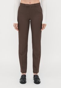 Brune skreddersydde bukser med en glatt tekstur, slim fit og flat front. Kombinert med svarte slip-on-sko.