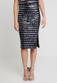Navy sequined dress with horizontal silver stripes, knee-length, fitted design, features a side slit, paired with silver strappy heels.