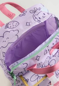 Lila ryggsäck med tecknade mönster, rosa remmar och grön dragkedja. Inre foder är lila och har en liten dragkedjeficka inuti.