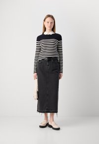 Fekete farmer szoknya, rojtos szegéllyel, amelyet egy sötétkék és krémcsíkos, hosszú ujjú inggel párosítanak, fehér gallérral. Bézs loafer cipő és táska.