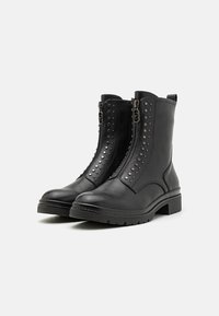 Schwarze Lederstiefeletten mit seitlichen Reißverschlüssen, Nietenakzenten und einer klobigen Sohle. Sie verfügen über eine glatte Textur und ein strukturiertes Design.
