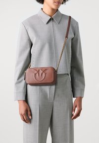Borsa a tracolla in pelle marrone con logo impresso, tracolla in catena dorata, forma rettangolare, cuciture a contrasto e finitura testurizzata.