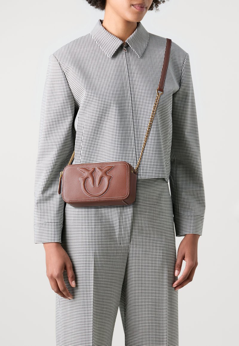 Borsa a tracolla in pelle marrone con logo impresso, tracolla in catena dorata, forma rettangolare, cuciture a contrasto e finitura testurizzata.