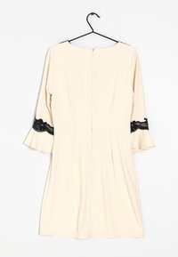 Beige klänning med utsvängda ärmar. Svarta spetsdetaljer vid ärmkanterna. Dragkedja bak. Slät tyg med en enkel skärning.