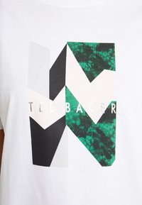 Camiseta blanca de algodón con un diseño geométrico que presenta formas en negro, verde y rosa claro, y el texto "TED BAKER" en letras plateadas.