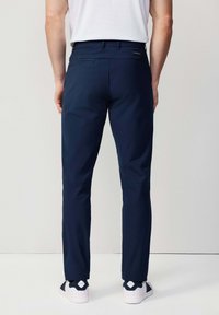 Pantalones azul marino ajustados hechos de una tela suave, con un bolsillo en la parte posterior y costuras sutiles, combinados con zapatillas blancas.
