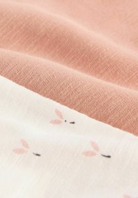 Nahaufnahme von weichem rosa und weißem Stoff mit kleinen gedruckten Kaninchen-Gesichtern auf dem weißen Abschnitt.