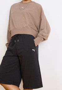 Brązowy krótki sweatshirt z prążkowanym dół, połączony z czarnymi szortami lounge z elastyczną talią i białym akcentem logo.