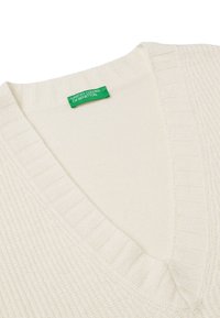 Cremfarbener V-Ausschnitt-Pullover mit geribbeltem Hals- und Saumabschluss, gestrickter Textur und einem grünen Etikett mit der Aufschrift "United Colors of Benetton."