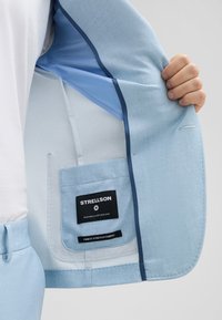 Helle blaue Sakko mit strukturiertem Stoff. Innenfutter in einem helleren Blau, mit einer Tasche und einem Etikett, das die "Strellson"-Marke zeigt.
