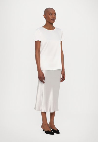 T-shirt branco de mangas curtas combinado com uma saia midi de seda prateada. Sapatos pretos de bico fino completam o visual. Design minimalista com texturas suaves.