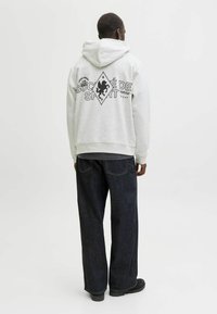 Szara bluza z kapturem z diamentowym, czarnym wzorem, "SOCIÉTÉ DE SPORT", w połączeniu z ciemnoniebieskimi dżinsami. Luźny krój i tekstura dresowa.