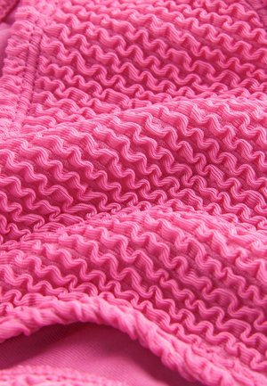 Tissu rose texturé avec un design à volants, présentant une finition douce et des motifs de vagues irréguliers pour plus de profondeur et de dimension.