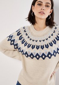 Suéter de punto color crema con un canesú de patrón en azul marino, azul claro y beige. Presenta un cuello redondo y un dobladillo acanalado.