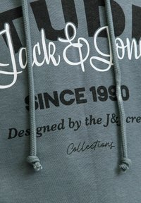 Hoodie gris avec un texte audacieux en noir et blanc. Comprend des cordons de serrage avec des extrémités texturées et une finition en matériau doux.