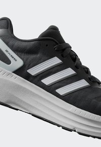 Zapatilla deportiva negra con parte superior texturizada, tres acentos en rayas blancas y una suela blanca gruesa con un agarre de patrón. Estilo: ZXRS.