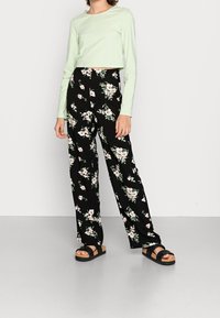 Vaaleanvihreä pitkähiha crop-top yhdistettynä mustiin leveälahkeisiin housuihin, joissa on vaaleanpunaisia ja valkoisia kukkia, ja mustat korolliset sandaalit.