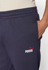 Σκούρες μπλε φόρμες από βαμβακερό μείγμα, με κόκκινο κεντημένο λογότυπο Puma και π λαϊνές τσέπες, με ρυθμιζόμενη μέση με κορδόνι.