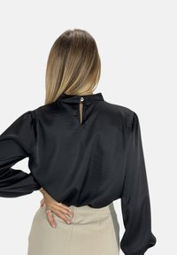 Blusa nera a maniche lunghe realizzata in un materiale simile alla seta, con un piccolo foro a chiave sulla schiena e dettaglio con bottone, caratterizzata da maniche a sbuffo e colletto alto.