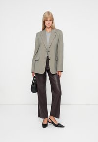 Szürke kockás zakó kivágott hajtókával, fekete gombokkal és zsebekkel; sötétbarna bőr nadrággal és fekete slingback magassarkúval párosítva.