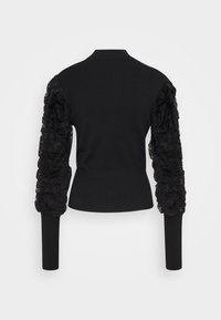 Musta neulepaita, jossa on vartalonmyötäinen leikkaus ja runsaat pitsireunaiset hihat, korkea kaulus ja ribbineulottu helma lisäämässä tekstuuria.