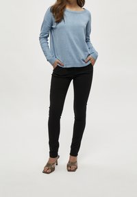 Vaalean sininen pitkähihainen villapaita rentoa mallia, jossa ribbikuvioiset hihansuut ja pyöristetty pääntie, yhdistettynä mustiin slim-fit-housuihin ja korkokenkiin.