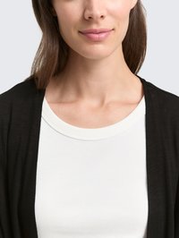 Zwarte cardigan over een witte ribbeltop. De cardigan heeft een zachte textuur en een losvallende pasvorm, met een ronde halslijn en gladde stof.