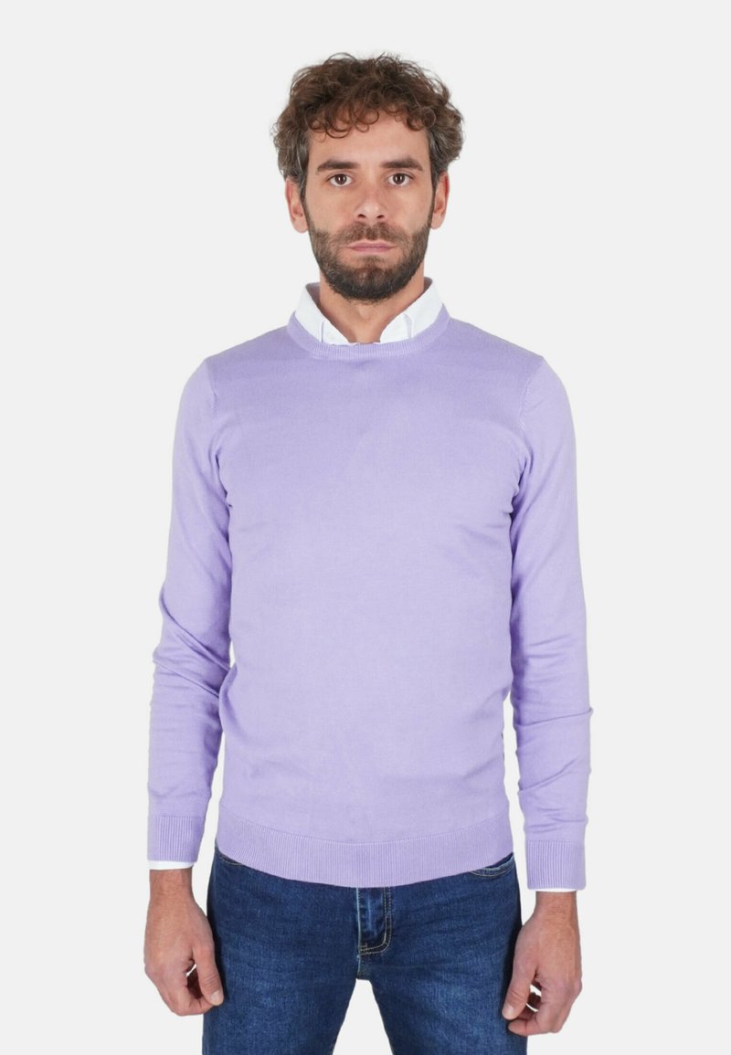 Maglione lilla realizzato in morbido tessuto a maglia, con scollo rotondo e polsini a coste. Indossato sopra una camicia bianca con colletto e abbinato a jeans blu.