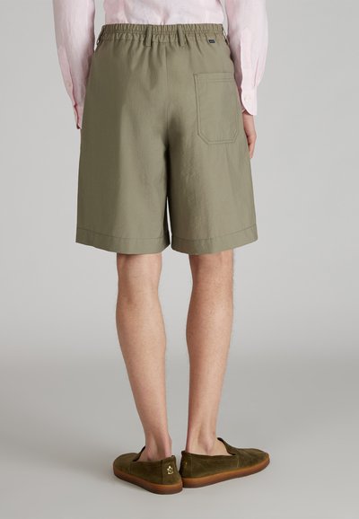 Jasnooliwkowe szorty z elastycznym pasem, z pojedynczą tylną kieszenią i prostym wykończeniem, w zestawie z brązowymi zamszowymi butami wsuwanymi.