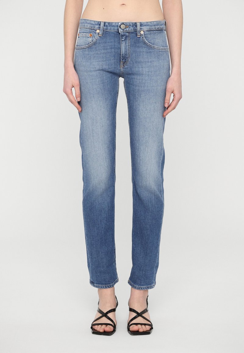 Light blue denim jeans with a straight leg fit, featuring front pockets, a button closure, and subtle fading. Paired with black strappy sandals.