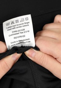 T-shirt di stoffa nera con un'etichetta di cura che mostra le istruzioni di lavaggio e i dettagli. L'etichetta è cucita al collo e mostra le informazioni sul prodotto.