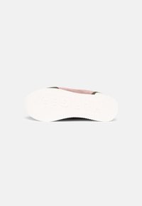 Suela de zapatilla blanca con un patrón de agarre texturizado y parte del upper en rosa y verde oliva visible sobre un fondo liso.