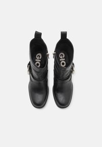 Botas de cuero negras hasta el tobillo con puntera redondeada, lengüetas en la parte superior, cremalleras laterales y una correa decorativa con un detalle de hebilla. Forro interior suave.