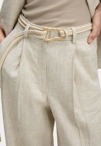 Pantaloni di lino beige con vestibilità ampia, caratterizzati da una cintura larga e una cintura in pelle color crema con una fibbia dorata decorativa.
