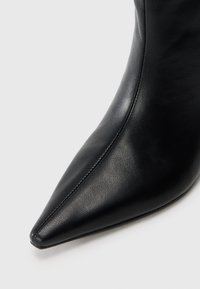 Black pointed-toe leather ankle boot with visible stitching along the front center, set against a plain light background.