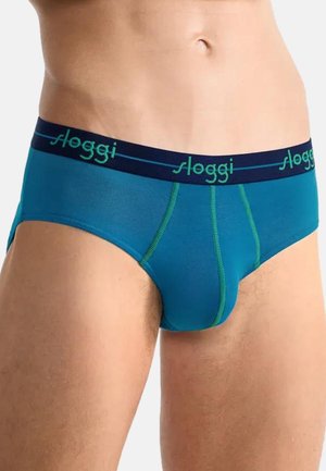 Male torso wearing teal briefs with navy waistband branded "sloggi" and green stitching detail against a neutral background.
