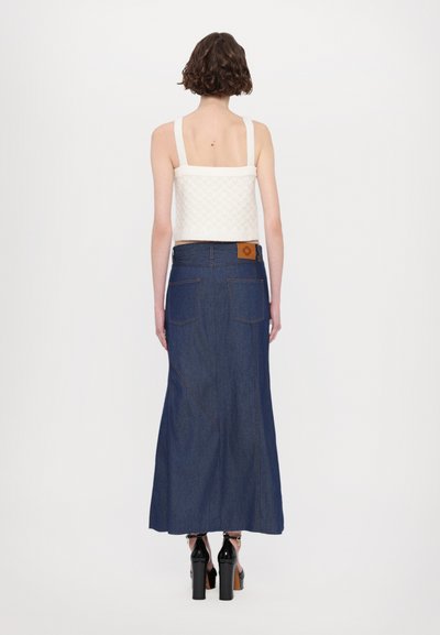 Valge kudumisest crop-top, millel on laiad rihmad, koos pika tumedast sinisest denimpükstega, millel on vöödimärgistus ja nähtavad õmblused taskutel.