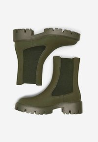 Bottes de cheville en caoutchouc vert avec panneaux élastiques sur les côtés, semelles à crampons épaisses et finition lisse. Le design présente des lignes épurées et une texture mate.